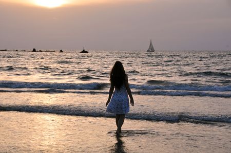 Teenager girl standing in a sea edge at sunset timeの写真素材