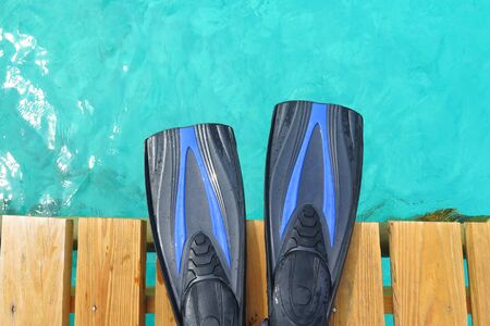 Blue scuba fins on the wooden pier over the blue ocean.の写真素材