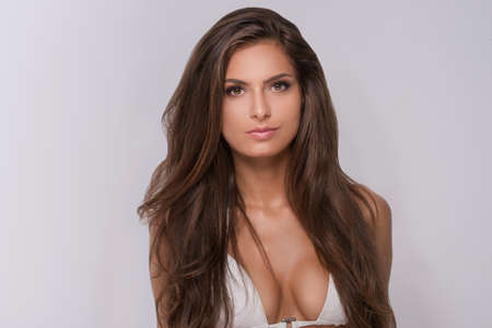 Beautiful woman in white bikini. Portrait of attractive young woman in white bra looking at camera while isolated on greyの写真素材