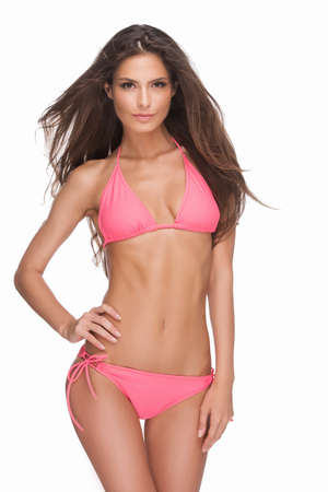 Beautiful fashion model. Attractive young woman in bikini looking at camera and holding hand on hip while standing isolated on whiteの写真素材