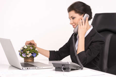 Talking at phone. Confident middle-aged businesswoman sitting at her working place talking at phoneの写真素材