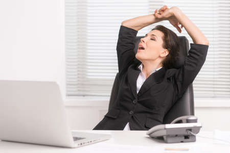 Businesswoman yawning. Tired middle-aged businesswoman sitting at her working place and yawningの写真素材