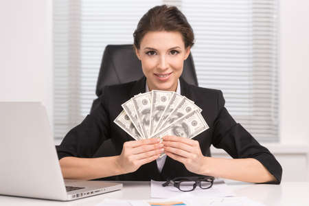 Successful businesswomen. Confident middle-aged woman sitting at her working place and holding money in her handsの写真素材