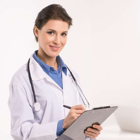 Confident female doctor. Confident middle-aged female doctor making notes at her note pad and looking at cameraの写真素材