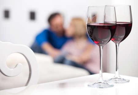 Romantic moments. Beautiful middle aged couple sitting on the floor and holding hands while two glasses of red wine standing on the foregroundの写真素材