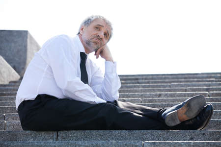 Depressed businessman. Sad senior man in formalwear sitting on stairs and holding his hand on chinの写真素材