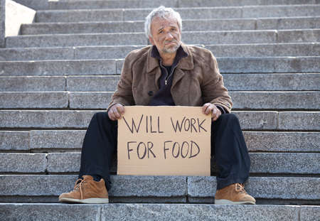 Will work for food. Depressed senior man sitting on stairs and holding posterの写真素材