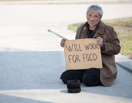 Will work for food. Depressed man in dirty wear sitting on the floor outdoors and holding posterの写真素材