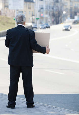 Depressed businessman. Rear view of senior man in formalwear standing on side of the road and holding posterの写真素材