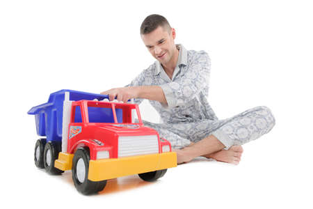 Big baby. Young man in pajamas playing with toy car while sitting isolated on whiteの写真素材