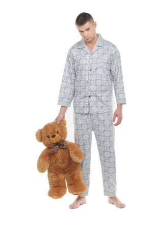 Man with teddy bear. Young man in pajamas holding teddy bear and looking at camera while standing isolated on whiteの写真素材