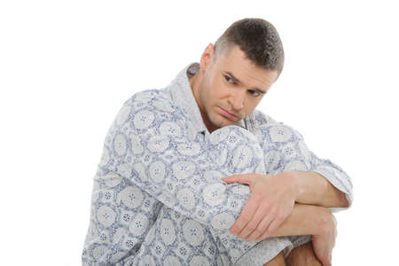 Sad man in pajamas. Depressed man in pajamas looking away while sitting isolated on whiteの写真素材