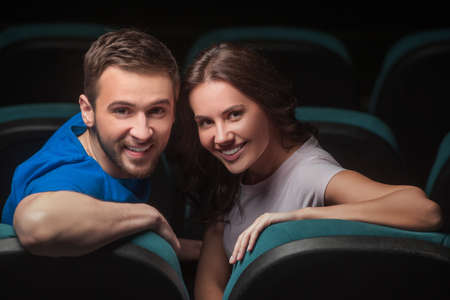 Couple at cinema. Young couple looking over shoulder while sitting at cinemaの写真素材