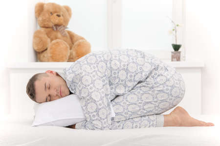 Big baby in pajamas. Side view of infant adult man lying on the baby bedの写真素材