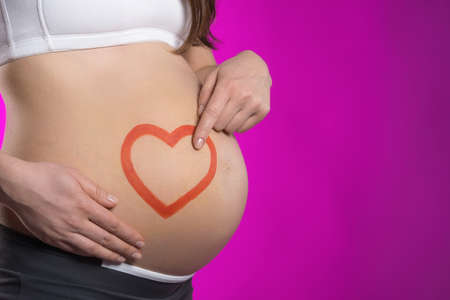 Pregnancy. Side view of pregnant woman touching her abdomen while standing against colored backgroundの写真素材