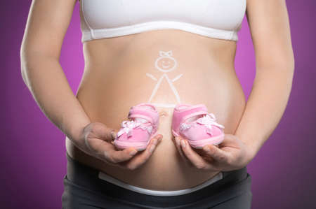 Pregnancy. Close-up of pregnant woman touching her abdomen while standing against colored backgroundの写真素材