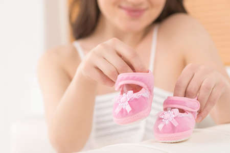Waiting for a baby. Close-up of young woman holding pink baby bootiesの写真素材