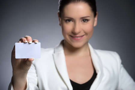 Businesswoman with business card. Confident middle-aged woman in formalwear holding business card and smiling while isolated on greyの写真素材