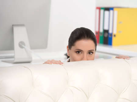 Businesswoman hiding. Frustrated middle-aged businesswoman looking out of the couchの写真素材