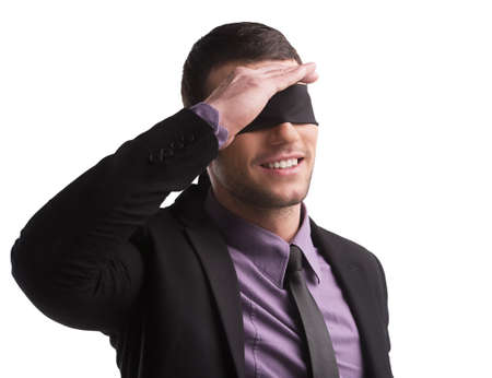 See nothing. Confident young businessman with ribbon covering his eyes holding his hand near eyes while isolated on whiteの写真素材
