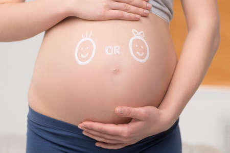 Pregnancy. Close-up of pregnant woman touching her abdomen with funny sketches on itの写真素材