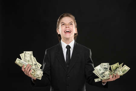 Power of the money. Little boy in formalwear holding money in his hands and making a face while standing against black backgroundの写真素材