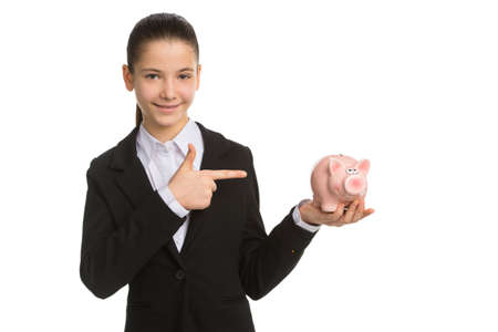 Little businesswoman with piggy bank. Cheerful little girl in formalwear holding piggy bank and pointing it while standing isolated on whiteの写真素材