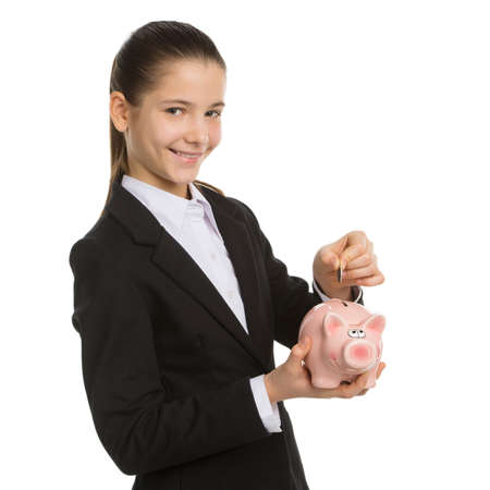 Little girl with piggy bank. Smiling little girl in formalwear holding piggy bank and putting coins in it while standing isolated on whiteの写真素材