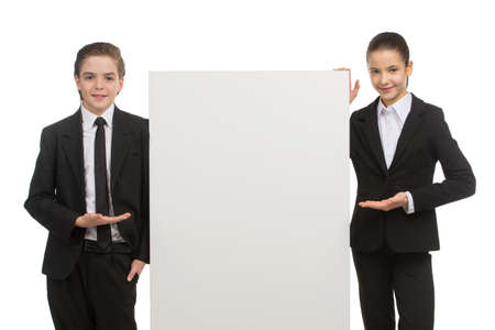 Little business kids. Cheerful little kids in formalwear pointing poster and smiling while standing isolated on whiteの写真素材