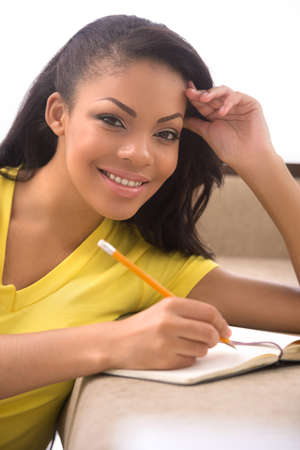 Woman making notes. Beautiful African descent women writing something in her note pad and looking at cameraの写真素材