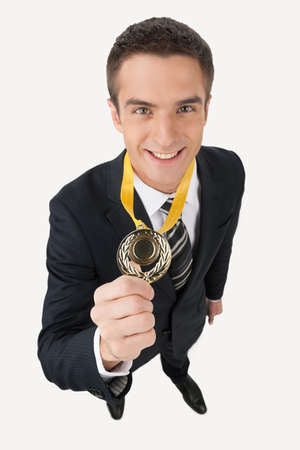 Business award. Top view of happy young businessman showing his gold medal while standing isolated on whiteの写真素材
