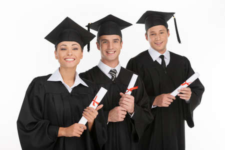 Graduating from the university. Three cheerful young people holding their diplomas and smiling at cameraの写真素材