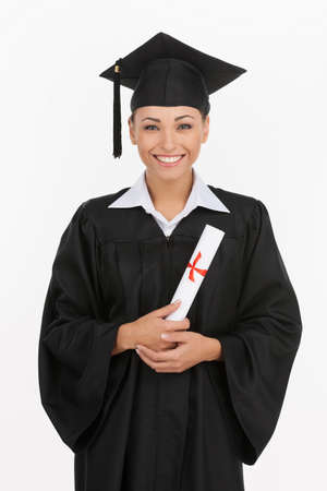 College degree. Happy young women in mortarboard holding diploma and smiling at camera while isolated on whiteの写真素材