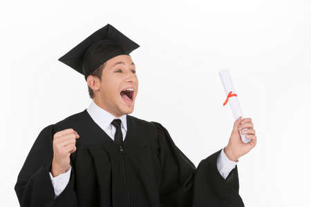 Happy grad. Happy young men in mortarboard holding diploma and gesturing while isolated on whiteの写真素材