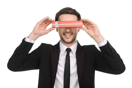 Young Businessman holding a gift box in front of his eyes and standing against white background