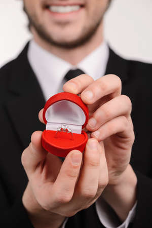 Young smiley men in suit holding an open box with engagement ring inside standing against white backgroundの写真素材