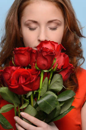 They smell so nicely. Attractive young woman smelling a bunch of red roses against blue backgroundの写真素材