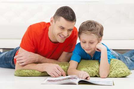 Father and son reading. Cheerful father and son reading magazine togetherの写真素材