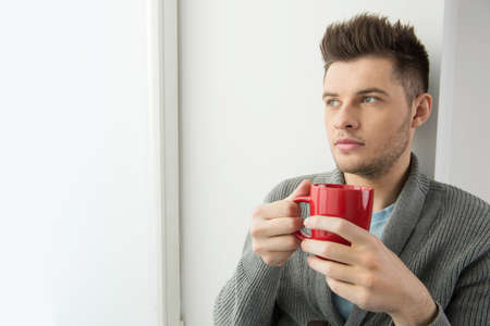 Men drinking coffee. Cheerful young men holding red cup and looking awayの写真素材