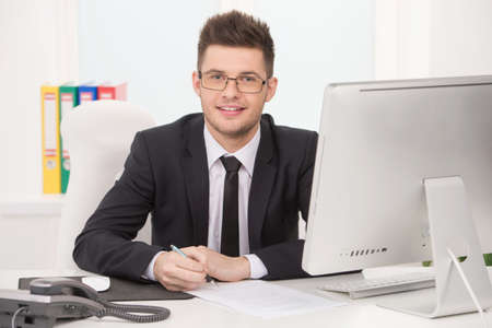 Confident businessman. Cheerful young man in formalwear sitting at his working place and looking at cameraの写真素材