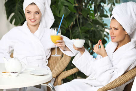 Girls in bathrobe drinking juice in spa salonの写真素材