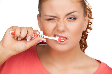 Brushing teeth. Portrait of young woman brushing her teeth while isolated on whiteの写真素材