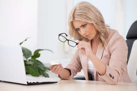 Woman in office. Beautiful young businesswoman sitting at her working place and holding glassesの写真素材