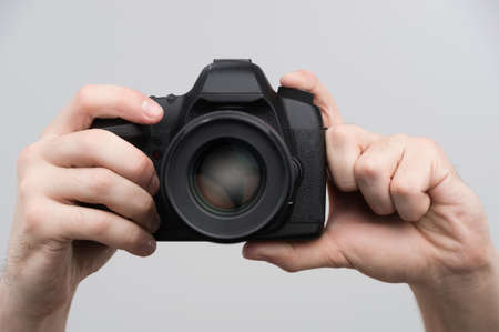 Camera in hands. Close-up of hands holding camera while isolated on greyの写真素材
