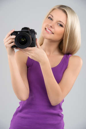 Woman with camera. Cheerful young women holding camera in her hands and smiling while isolated on greyの写真素材