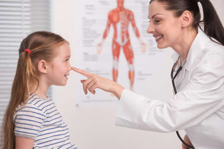 Doctor and little girl. Cheerful young doctor touching little girl nose and smilingの写真素材
