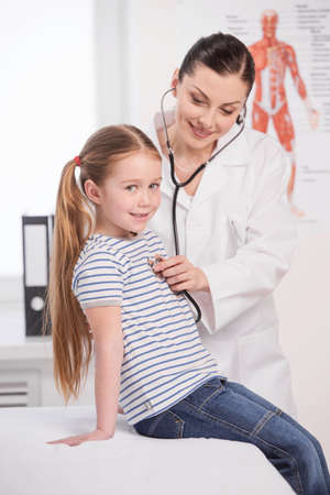 Doctor and little girl. Cheerful young doctor coat examining little girlの写真素材