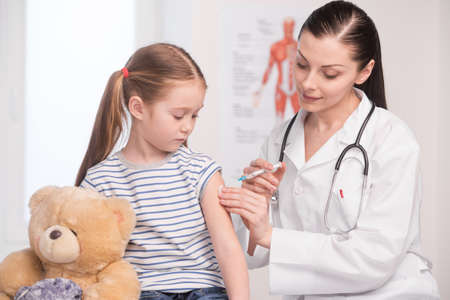 Injection. Confident young doctor in lab coat doing injection to a little girl