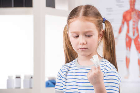 Injured finger. Sad little girl looking at her injured finger