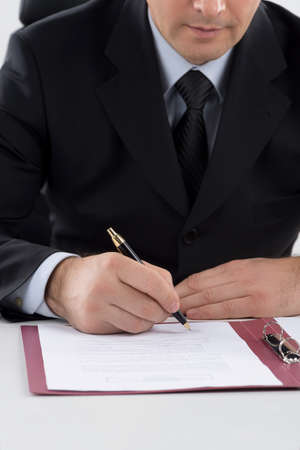 Signing documents. Cropped image of middle-age man in formalwear signing documents while sitting at...